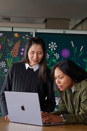 Due persone del team Marketing di Apple che collaborano su un MacBook di fronte a poster realizzati dal loro team.