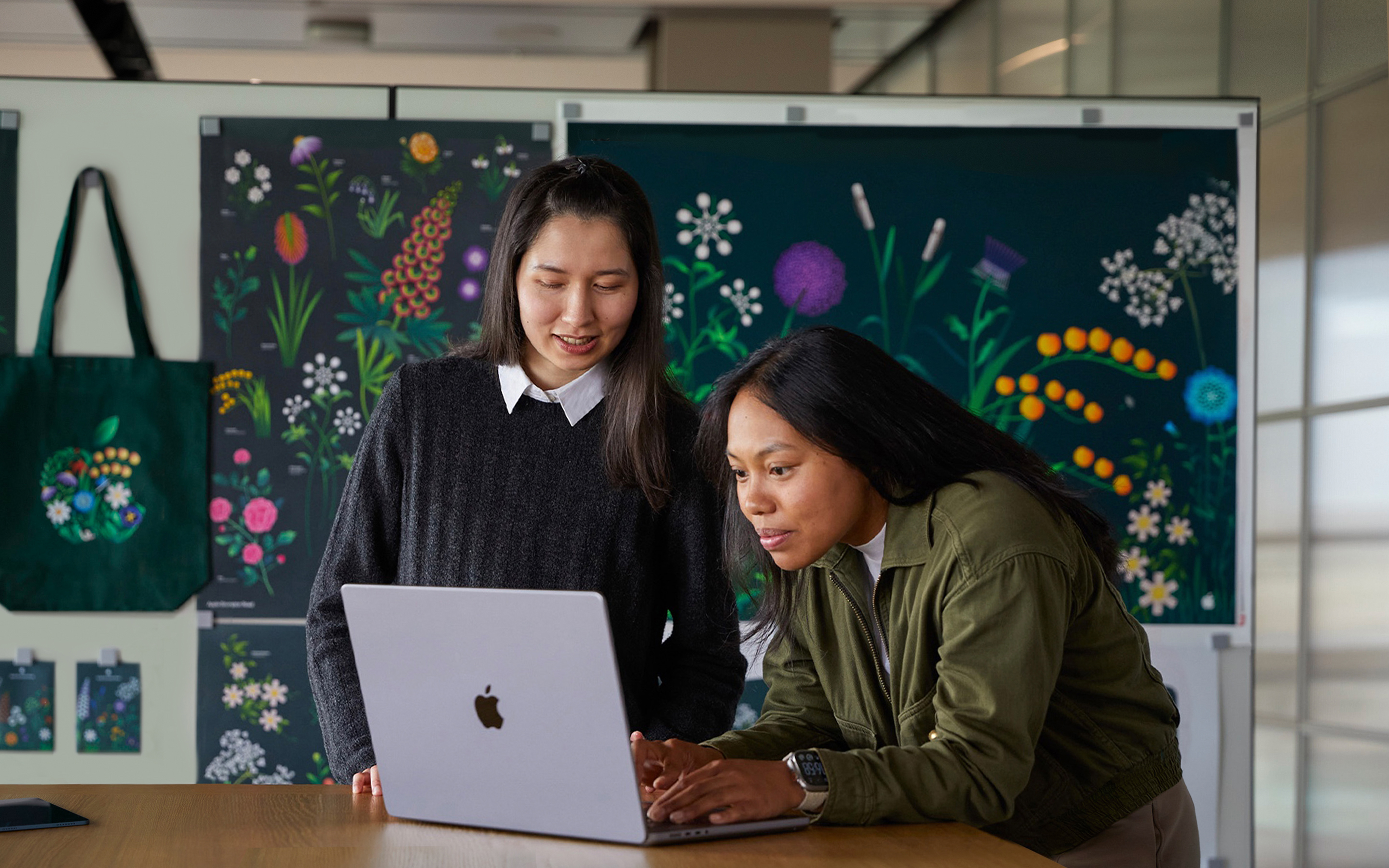 Dva členové týmu Marketing ve společnosti Apple spolupracují na MacBooku před plakáty navrženými jejich týmem.