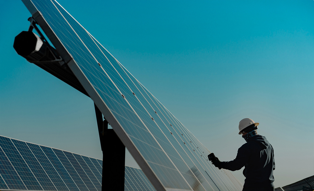 Ein Mann mit Schutzhelm arbeitet an einer großen Solaranlage im Freien.