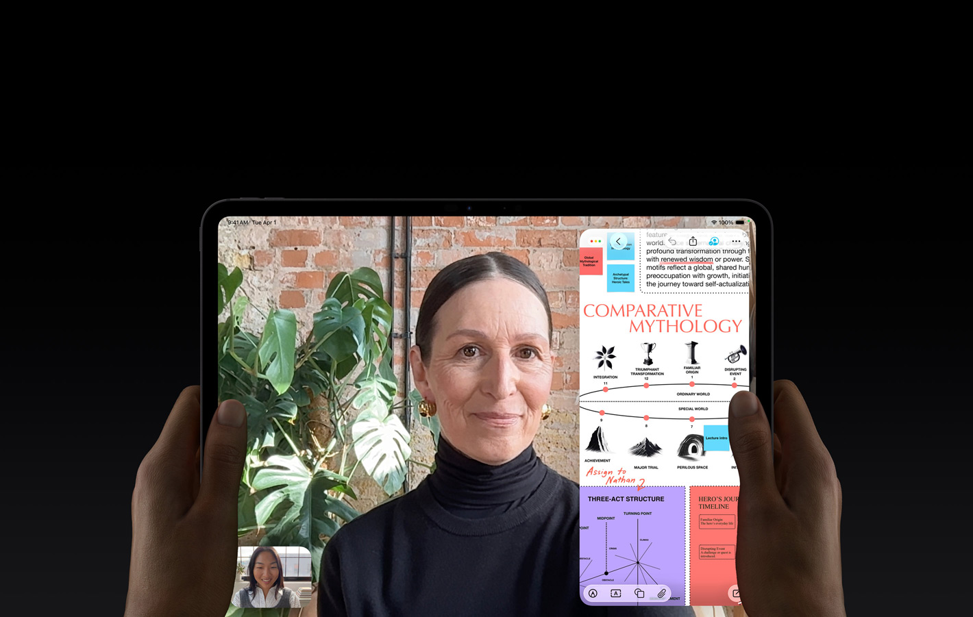 iPad Pro, front exterior, space black color, left and right hands holding in landscape orientation, rounded corners, black display bezel, display showing a FaceTime conversation being live translated, and an educational app showing a presentation of 'Comparative Mythology' with text, diagrams, and handwritten notes