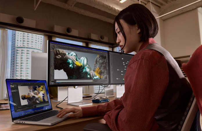 Eine Person, die in einem Büro mit einem MacBook Pro arbeitet, das mit einem Studio Display XDR verbunden ist