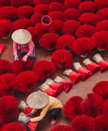 Photo of two workers drying bright red bundles of incense