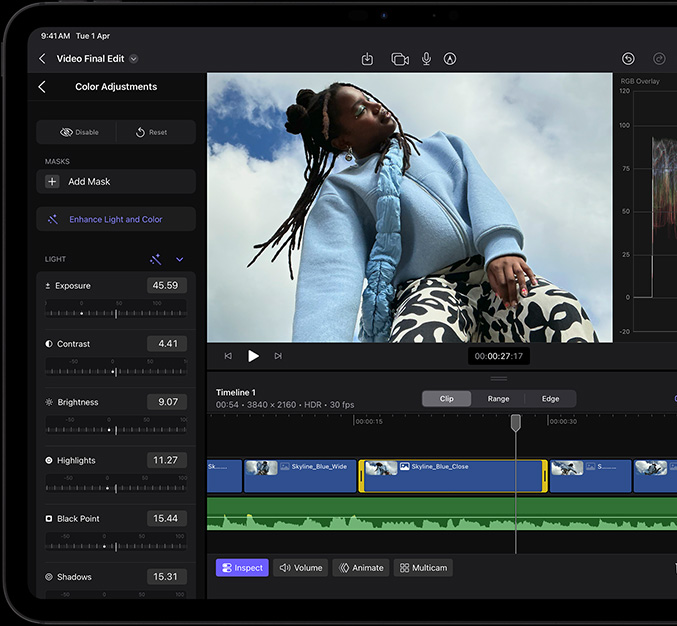 iPad Pro, front exterior, black display bezel, display showing video editing app with a picture of a model in a blue coat and black-and-white printed pants, colour adjustment panel open on the left with various video effects and sliders, timeline at the bottom with multiple video clips and audio tracks