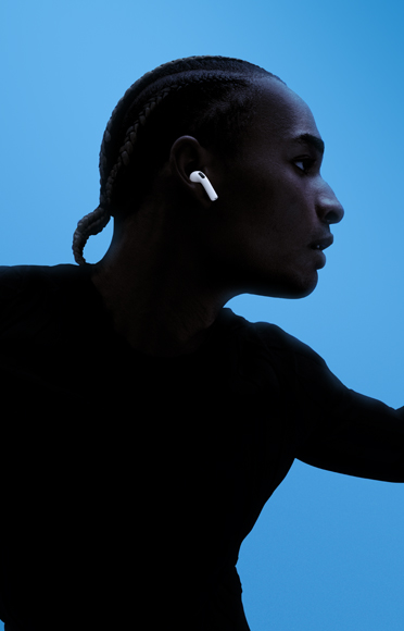 Una persona che indossa gli AirPods 5, con le braccia aperte, su uno sfondo colorato