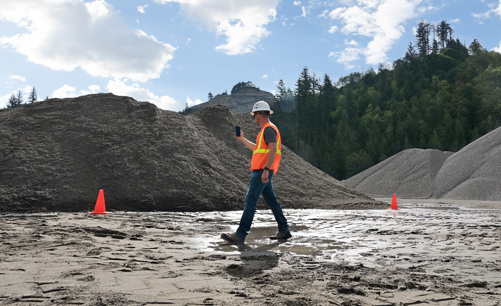 A field worker uses an iPhone to assess a work site while walking across muddy terrain