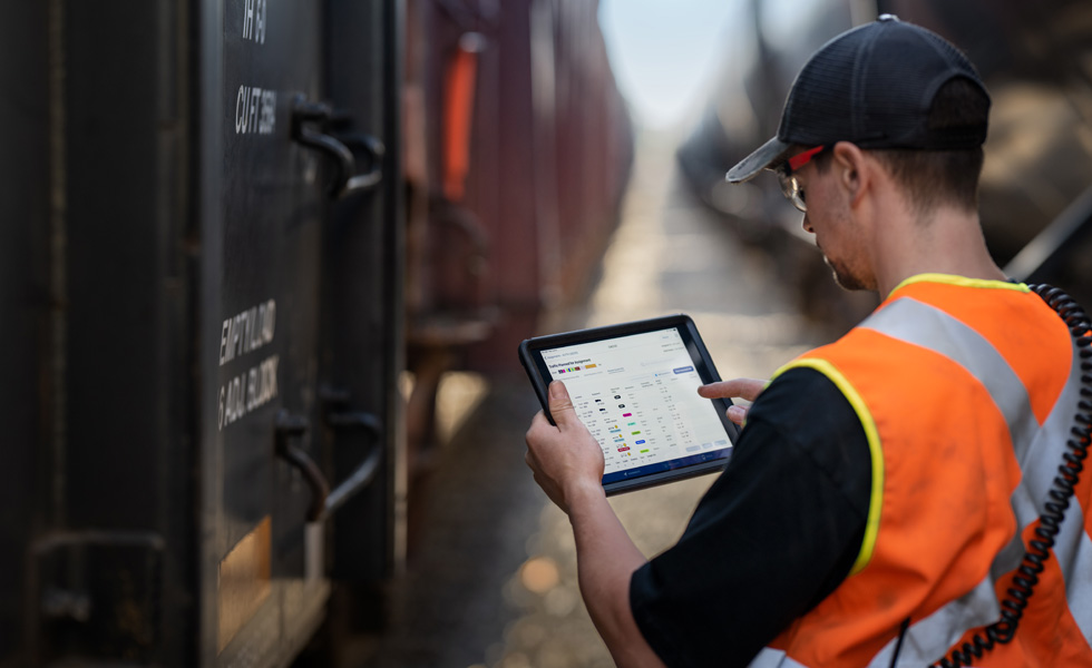 A railroad worker stands beside a train checking an iPad that displays scheduling information