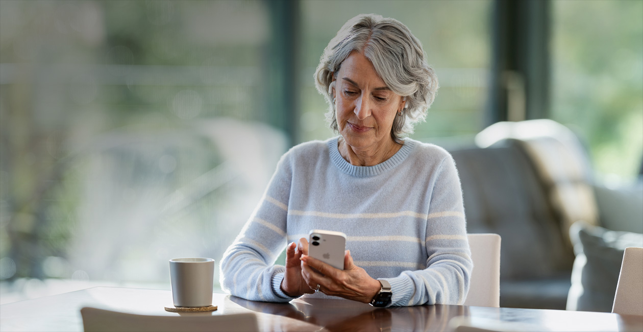 An older woman looking at her iPhone at the table.