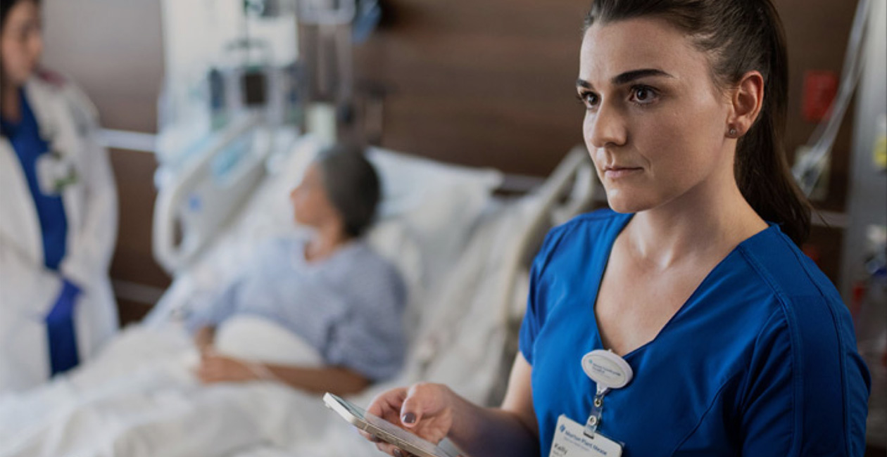A nurse texting on her iPhone while another provider speaks to a patient.