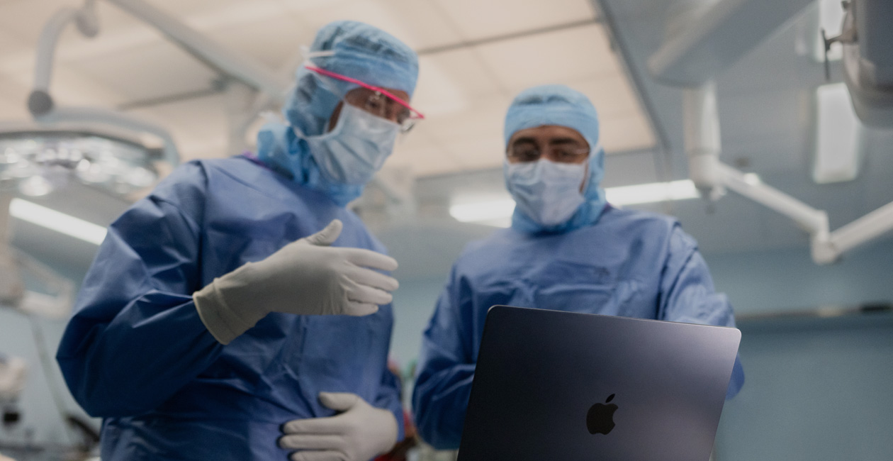 Two surgeons discussing something on the screen of a MacBook Pro in the operating room.