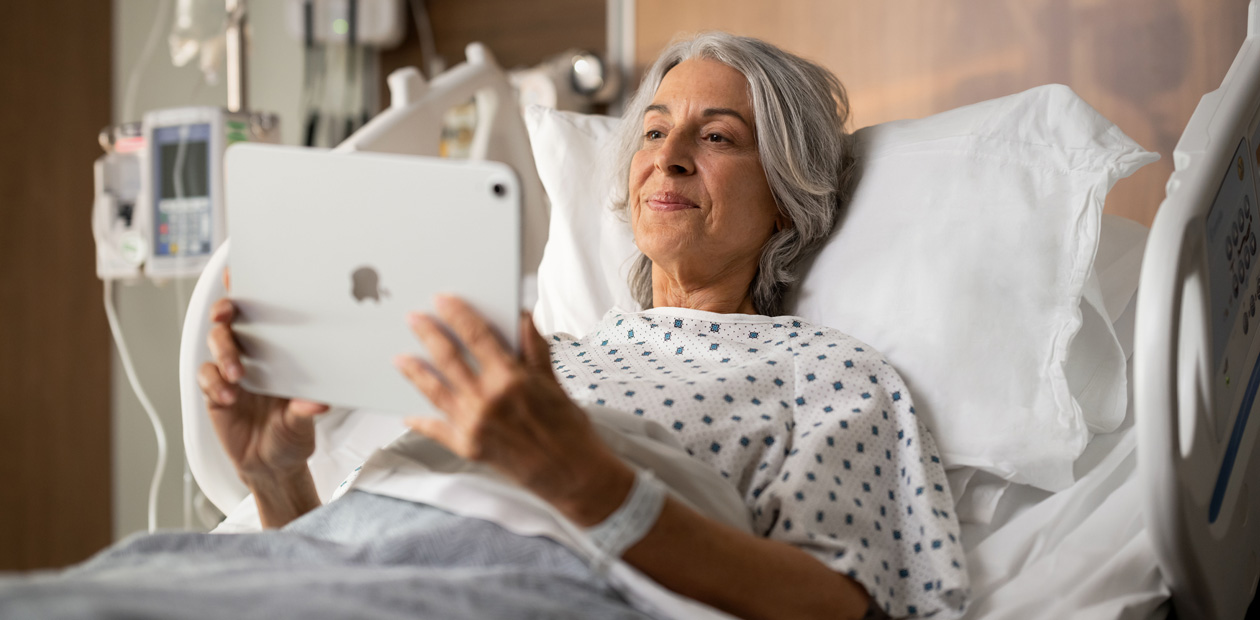 Una paziente sdraiata in un letto d’ospedale mentre guarda il suo iPad.