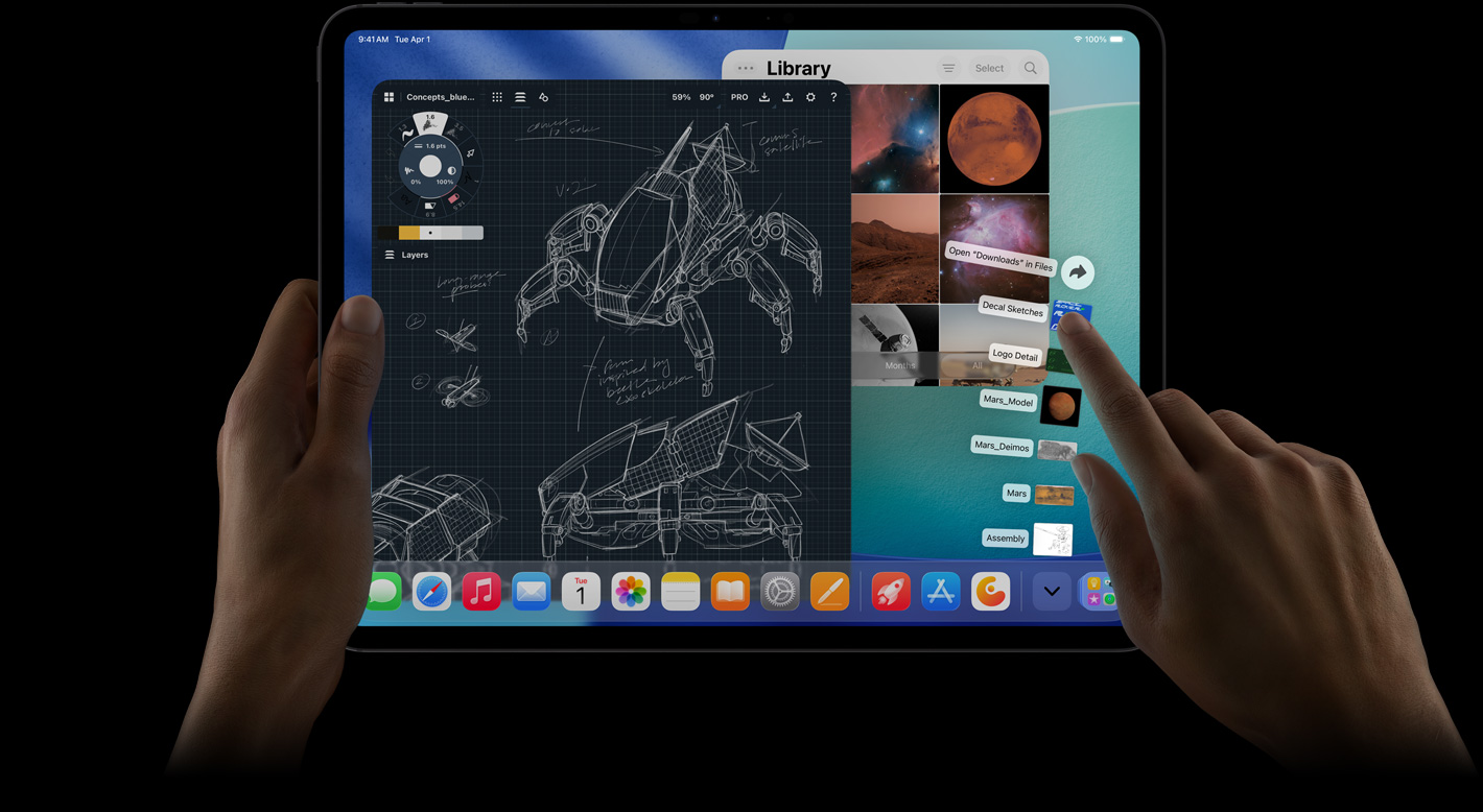 iPad Pro, front exterior, landscape orientation, right hand gesturing over Downloads folder files fanned out, display showing iPadOS 26 interface with multiple open apps including photo editing app with detailed robot blueprints and handwritten annotations and multiple design stages, and Photos Library