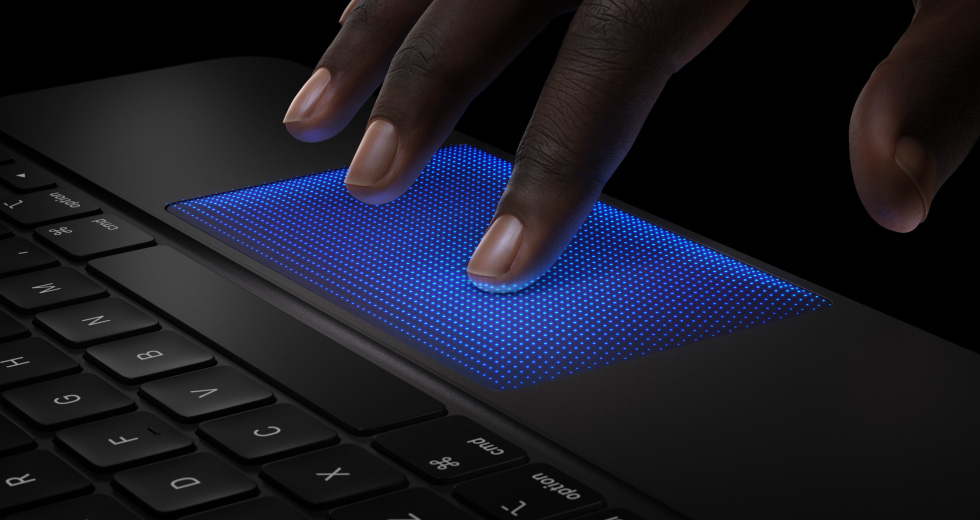 Lateral do Magic Keyboard preto, mostrando uma mão com os dedos sobre o trackpad, com o indicador em uma sombra azul indicando o gesto de toque