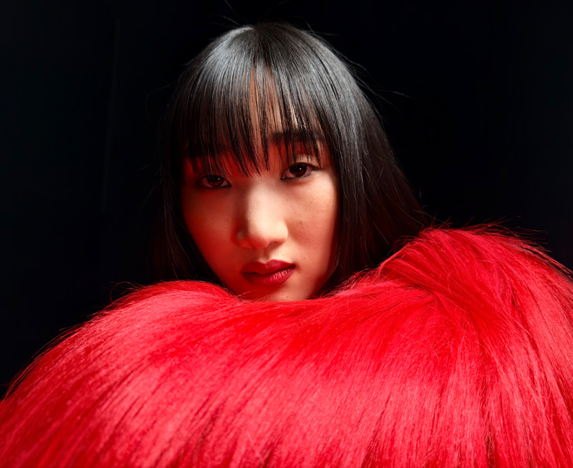 A close-up of a woman wearing a bright red feather top demonstrates the super-high-resolution photographic capabilities on iPhone 17 Pro