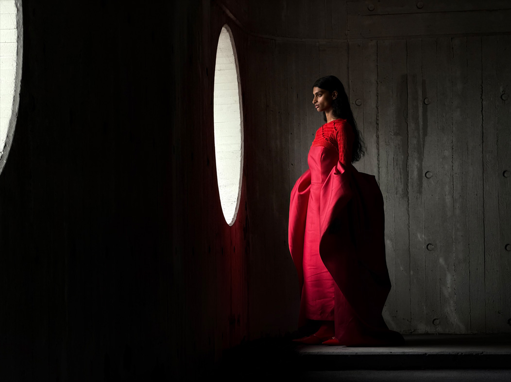 A woman wearing a long red dress stands in an empty room being photographed. The Photo app toggles through the following focal lengths to demonstrate the capabilities of the pro camera system: 200 mm, 100 mm, 48 mm, 35 mm, 28 mm, 13 mm, and macro