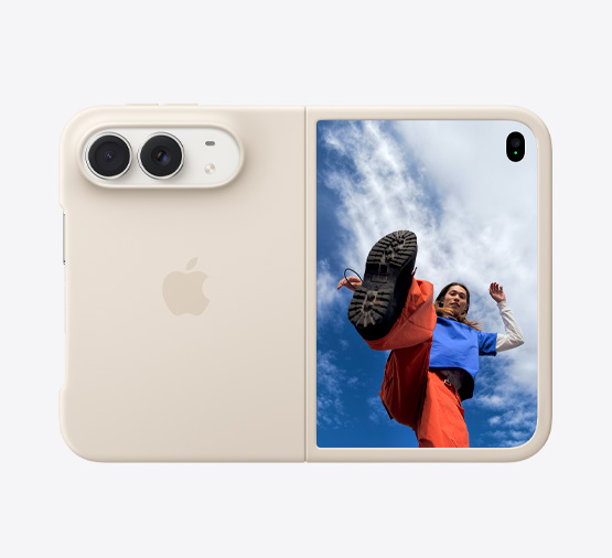 iPhone Duo, warna Putih Star White dalam Casing Silikon Krem Pasir, orientasi lanskap, terbuka sepenuhnya secara horizontal, kamera Dual Fusion di kiri atas, casing menutupi eksterior belakang dan tepi luar layar depan, sisi kanan menampilkan layar luar dengan gambar seseorang berdiri di bawah langit biru yang penuh awan