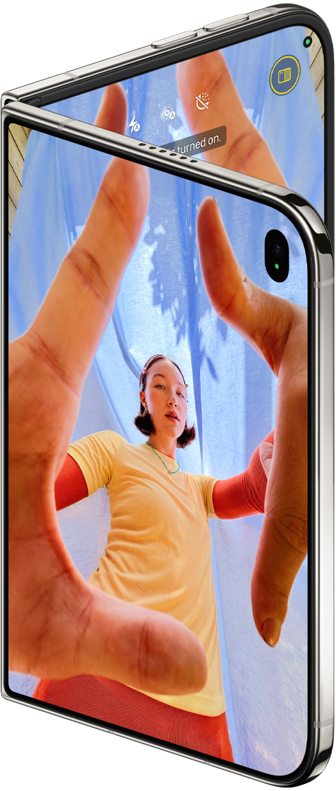 iPhone Duo, warna Putih Star White, sedikit terbuka, aplikasi Kamera pada layar luar dengan kamera depan Center Stage, layar dalam menampilkan perpustakaan aplikasi Foto