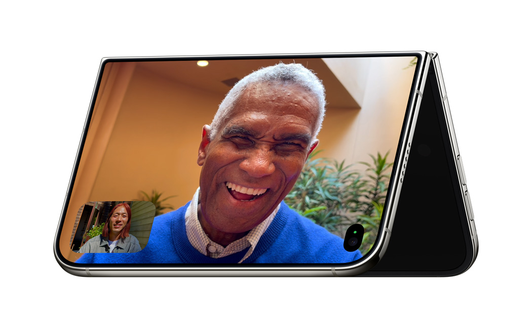 iPhone Duo yang ditopang dalam posisi V terbalik dan diletakkan bertumpu pada tepiannya dengan layarnya menghadap ke luar dalam mode Siaga dengan aplikasi FaceTime