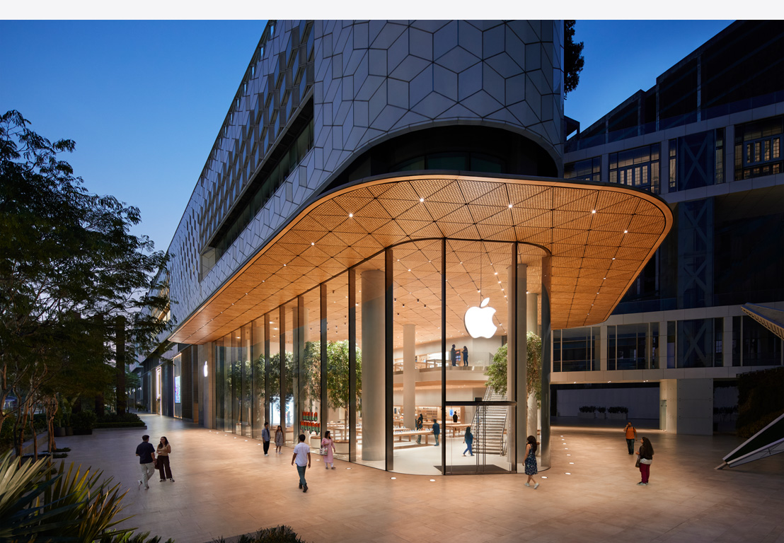 Apple store at night, glass windows, lit up inside, Apple logo centered on top of front door.