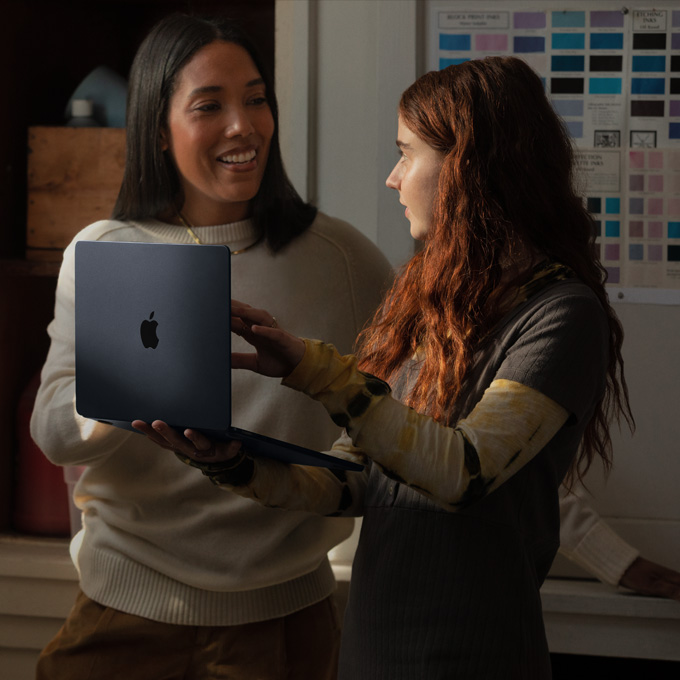 A teacher and a student have a conversation while holding a MacBook laptop