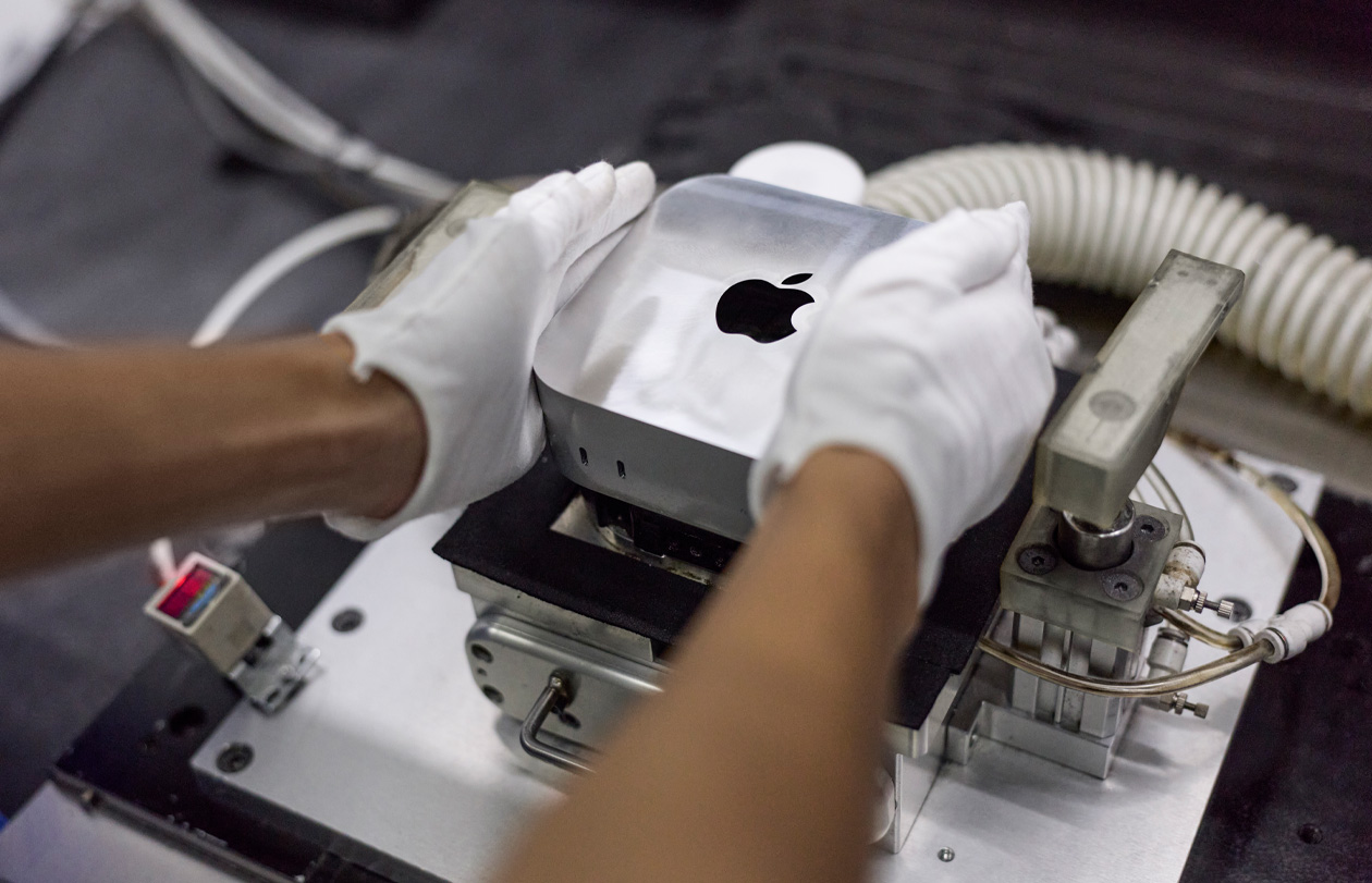 Gloved hands placing a Mac mini into a manufacturing machine during assembly
