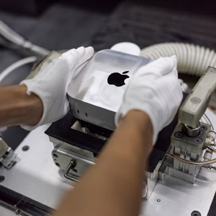 Gloved hands placing a Mac mini into a manufacturing machine during assembly
